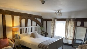 Un dormitorio con una cama blanca, cabecera de madera, mesita de noche, lámpara, silla y un espejo grande.