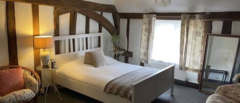 Ein Schlafzimmer mit einem weißen Bett, einem Holzkopfteil, einem Nachttisch, einer Lampe, einem Sessel und einem großen Spiegel.