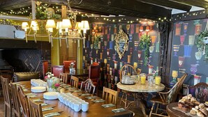 Un comedor con mesas y sillas de madera, una araña y un papel tapiz estampado.