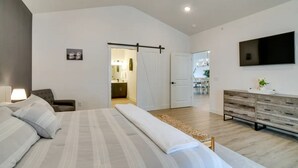 A modern bedroom with a large bed, a bedside table with a lamp, a wooden dresser, and a TV mounted on the wall. - Branson Vacation Rental w/ Table Rock Lake Views!  (Branson)