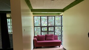 A room with a large window, a red sofa, and a patterned ceiling. - Mpanga Nature Center  (Mpigi)