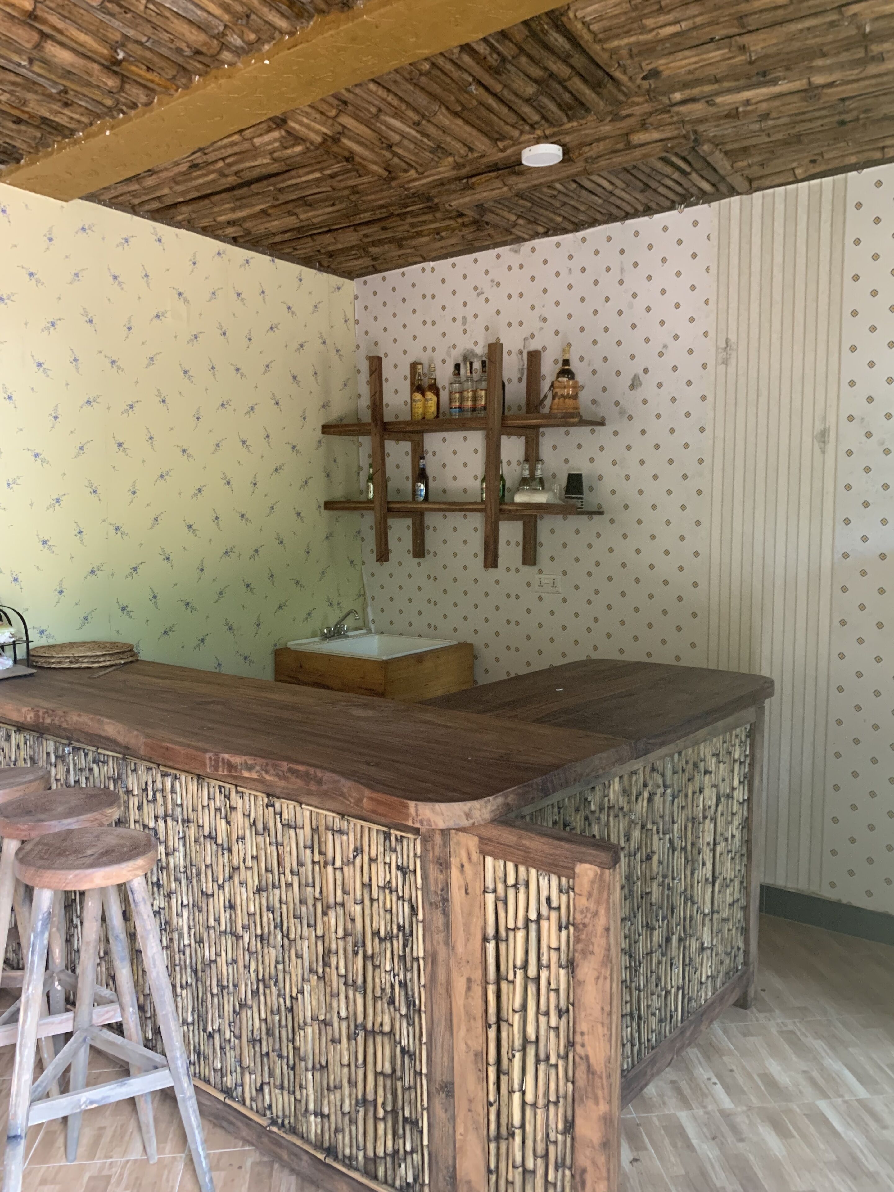 A bar area with a wooden counter, stools, and shelves with bottles.