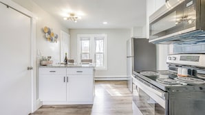 A modern kitchen with white cabinetry, a central island, a stainless steel stove, and a large window providing natural light. - Weymouth Apartment: Close to Beaches & Boston! (Weymouth)