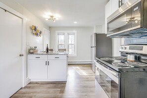Una cocina moderna con armarios blancos, una isla central, una estufa de acero inoxidable y un amplio ventanal que proporciona luz natural.