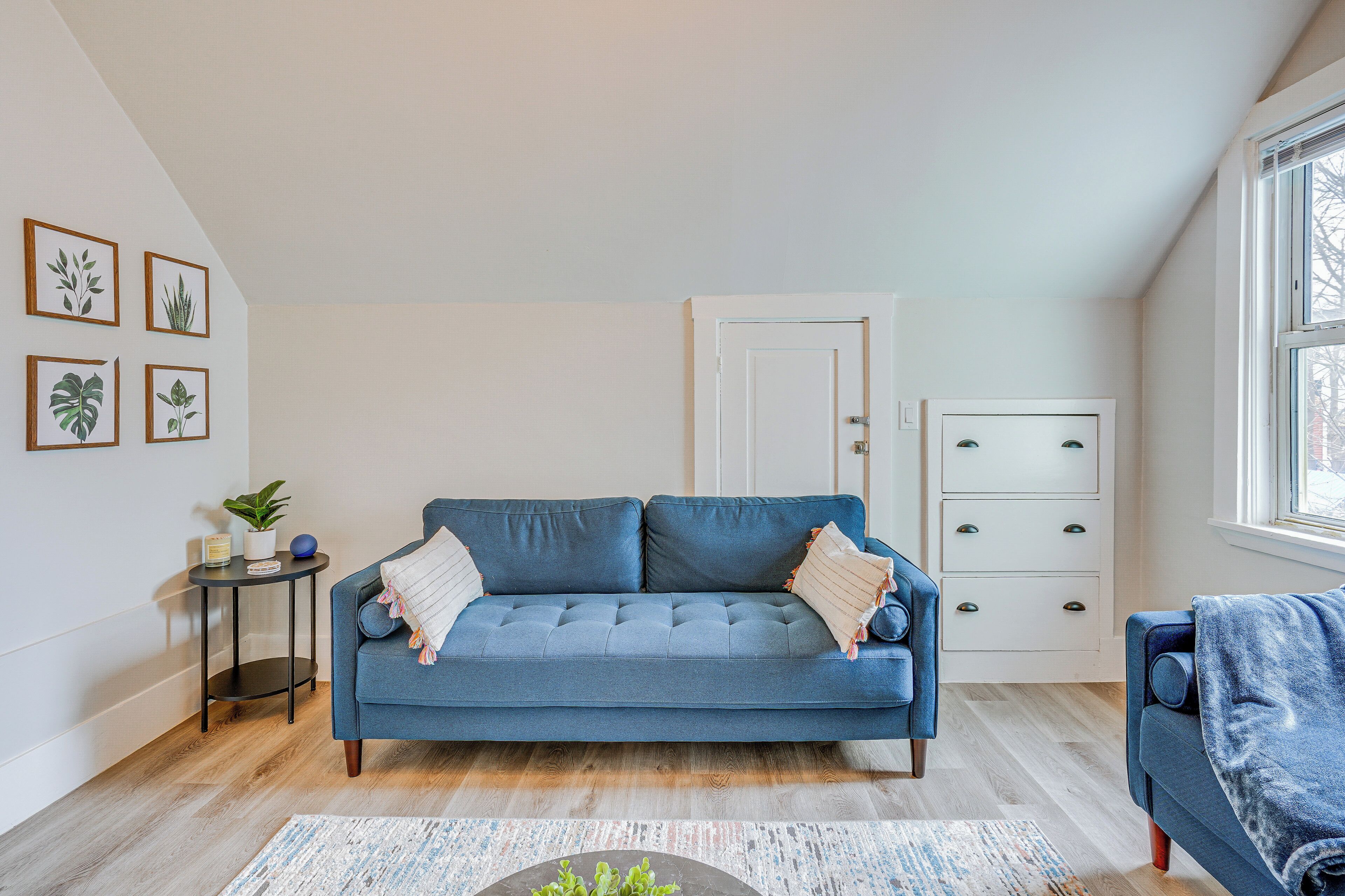 Una sala de estar con un sofá azul, una mesita auxiliar con una planta y una puerta con cajones.