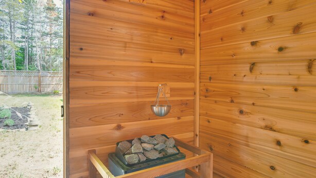 A wooden cabin interior with a fireplace, a metal container on the mantel, and a view of the outdoors. - 'The I House' Interlochen Home w/ Sauna, Fireplace (Interlochen)