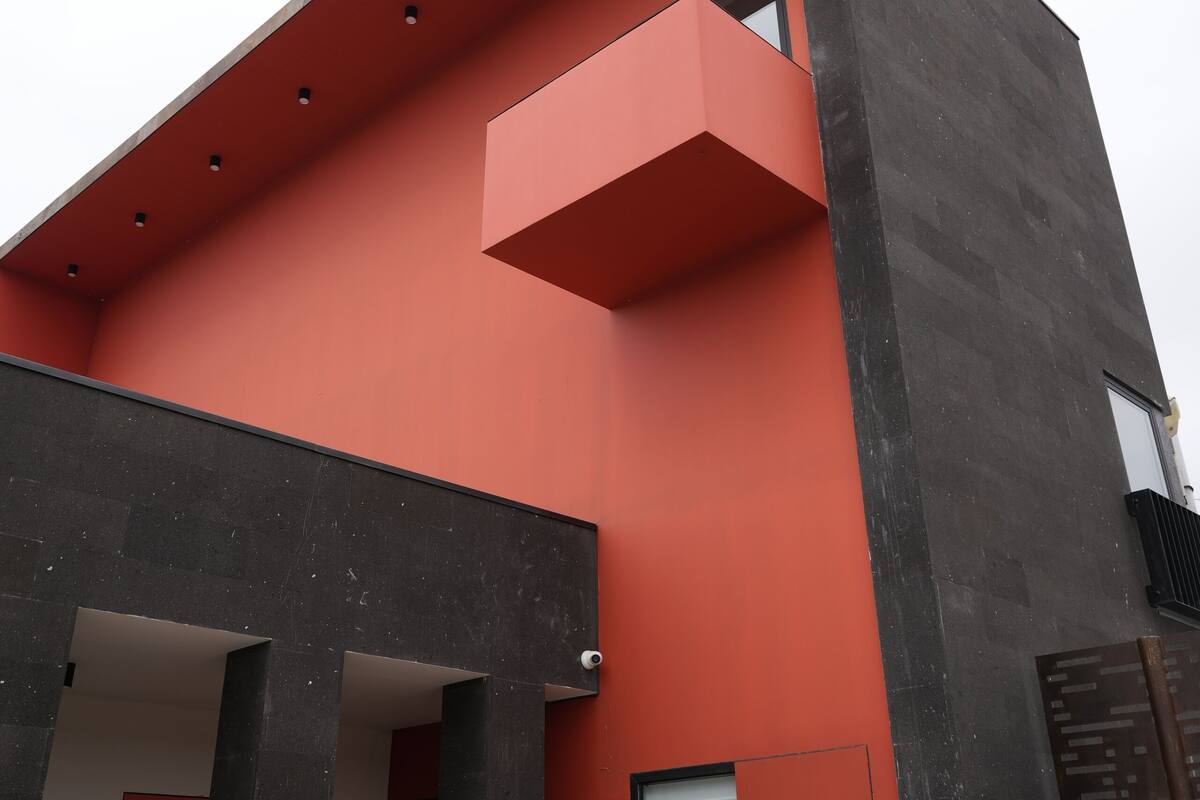 Ein modernes Gebäude mit roter Fassade, schwarzen Säulen und einem Balkon.