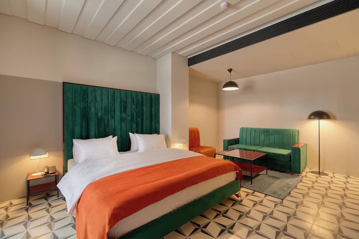 Ein modernes Hotelzimmer mit einem großen Bett, einem grünen Polstersofa, einem kleinen Tisch und einem gemusterten Boden.