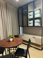 Um quarto com uma mesa redonda de madeira, cadeiras pretas, uma planta em vaso, um banco embutido com espaço de armazenamento e um armário com frente de vidro.
