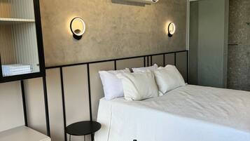 Un dormitorio moderno con cama, mesitas de noche, una mesa redonda de madera y aire acondicionado de pared.