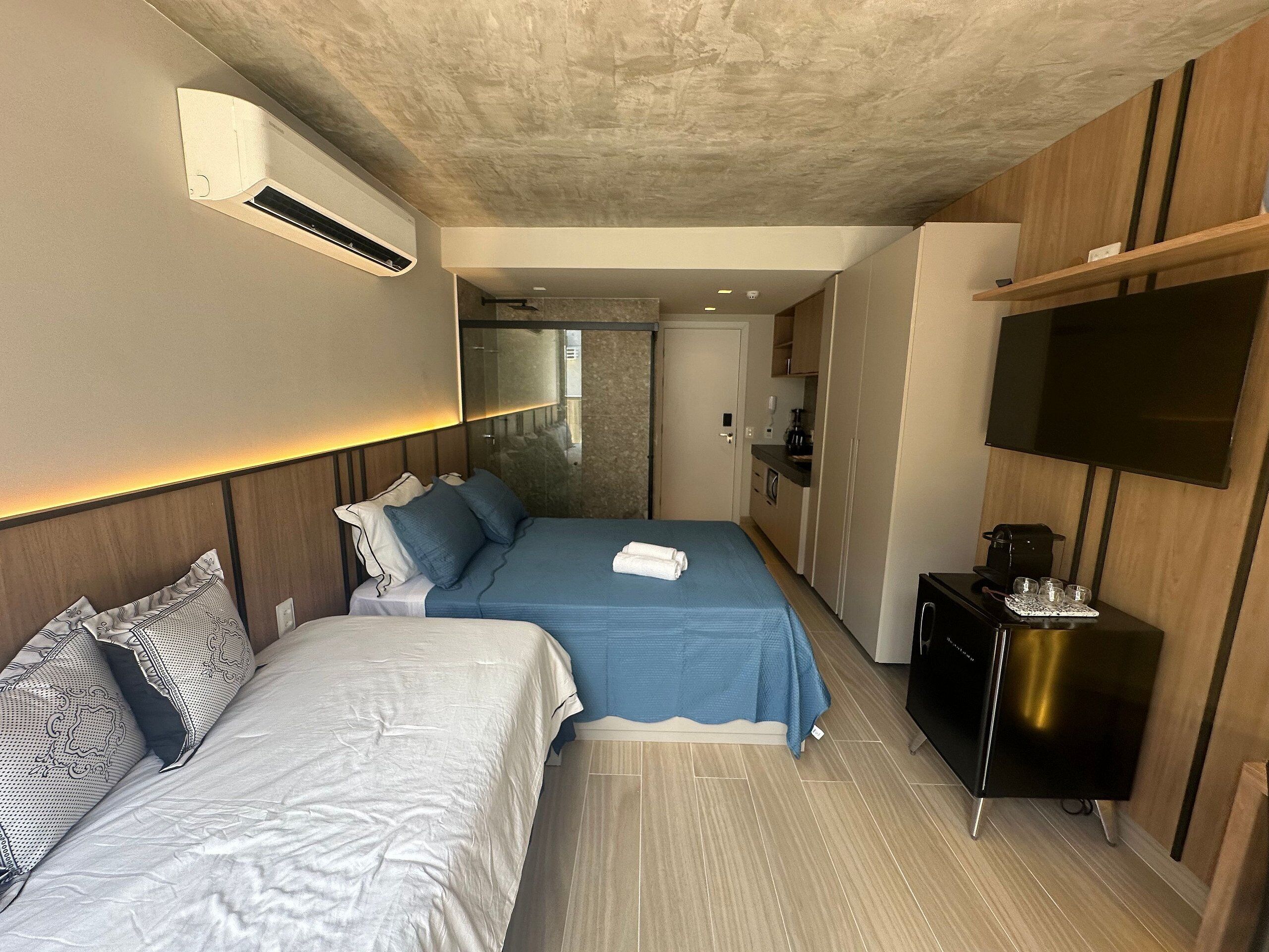 A hotel room with two beds, a TV, a coffee maker, and a minibar.