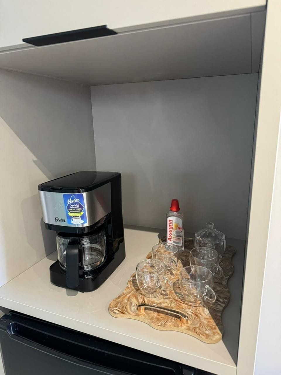 A coffee machine, a bottle of syrup, and several glasses on a shelf.