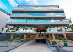 Een meerlaags gebouw met een modern architectonisch ontwerp, voorzien van балконы met glazen leuningen en buiten zitplaatsen.