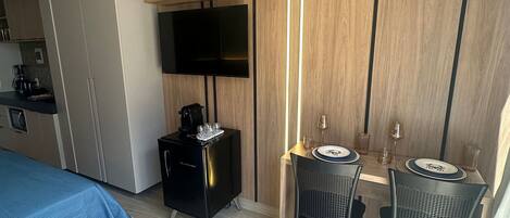 A hotel room with a bed, a desk with two chairs, a TV mounted on the wall, and a coffee machine.