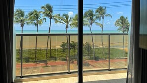 Een kamer met een groot raam, uitzicht op een strand met palmbomen en een heldere lucht.