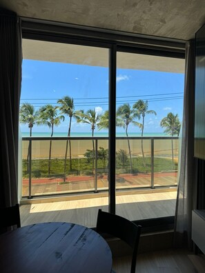 Een kamer met een groot raam, uitzicht op een strand met palmbomen en een heldere lucht.