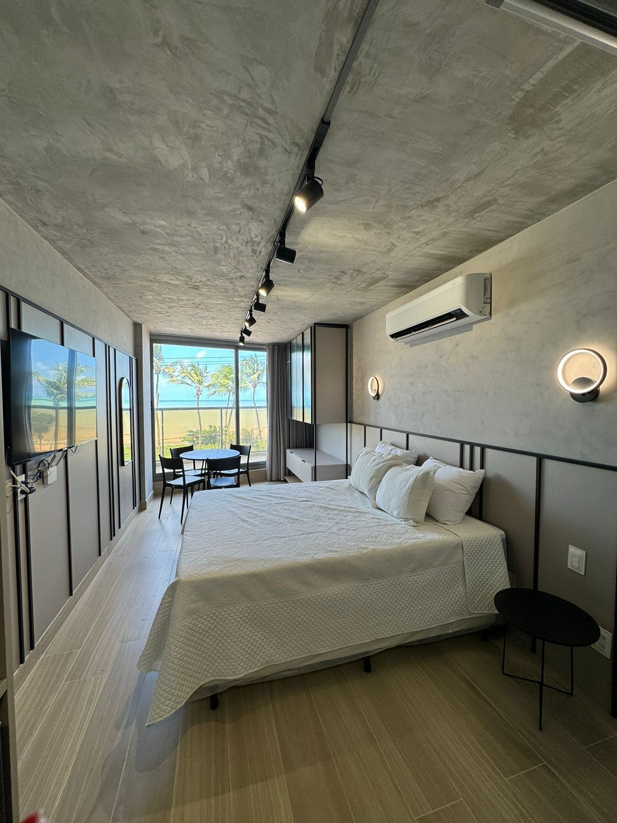 Un dormitorio moderno con una cama grande, un escritorio, una silla, un televisor y un equipo de aire acondicionado.