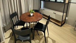 Een eetgedeelte met een ronde tafel, vier stoelen, een potplant, een inbouwbank en een groot raam met jaloezieën.