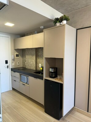 Une cuisine compacte équipée d’un réfrigérateur intégré, d’une machine à café et d’une plante en pot posée sur le plan de travail.
