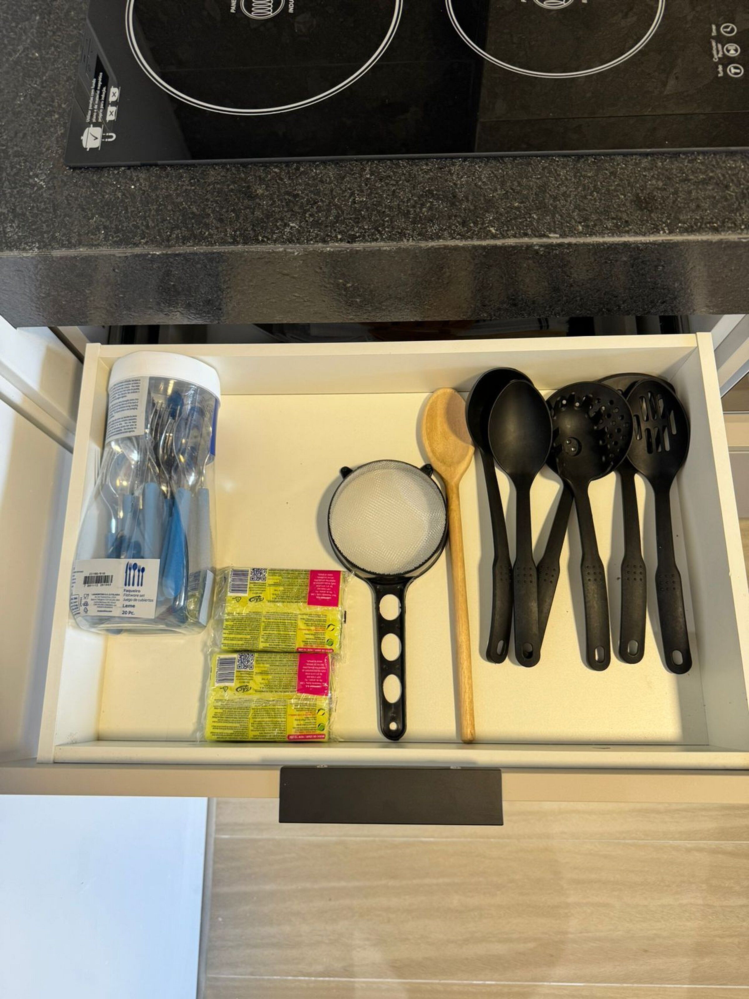 A drawer with kitchen utensils, a strainer, and packaged food items.