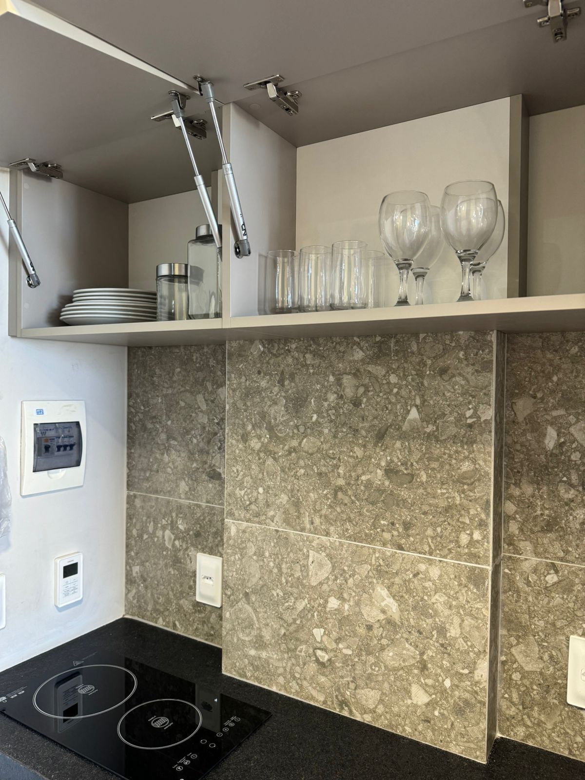 Cozinha moderna com fogão por indução preto, painel de fundo em granito e acessórios de aço inoxidável.