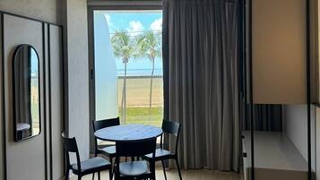 Una habitación moderna con una mesa redonda, cuatro sillas, un ventanal con vistas a palmeras y un techo con vigas a la vista.