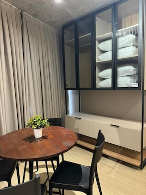 A room with a round wooden table, black chairs, a potted plant, a built-in bench with storage, and a glass-fronted cabinet. - Setai Yacht Suítes (João Pessoa)