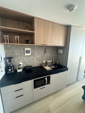 A modern kitchen with a black countertop, wooden cabinets, a built-in microwave, and a coffee machine. - Setai Yacht Suítes (João Pessoa)