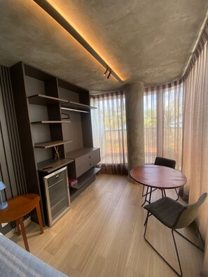 Une chambre moderne dotée d’un meuble de rangement intégré pour les appareils multimédias, d’une table à manger avec des chaises et d’une grande fenêtre avec des rideaux.