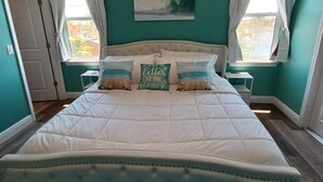 A bedroom with teal walls, a large bed with a white quilt, two nightstands, and a window with curtains. - Newly remodeled gulf canal home w/floating dock and kayaks (Hernando Beach)