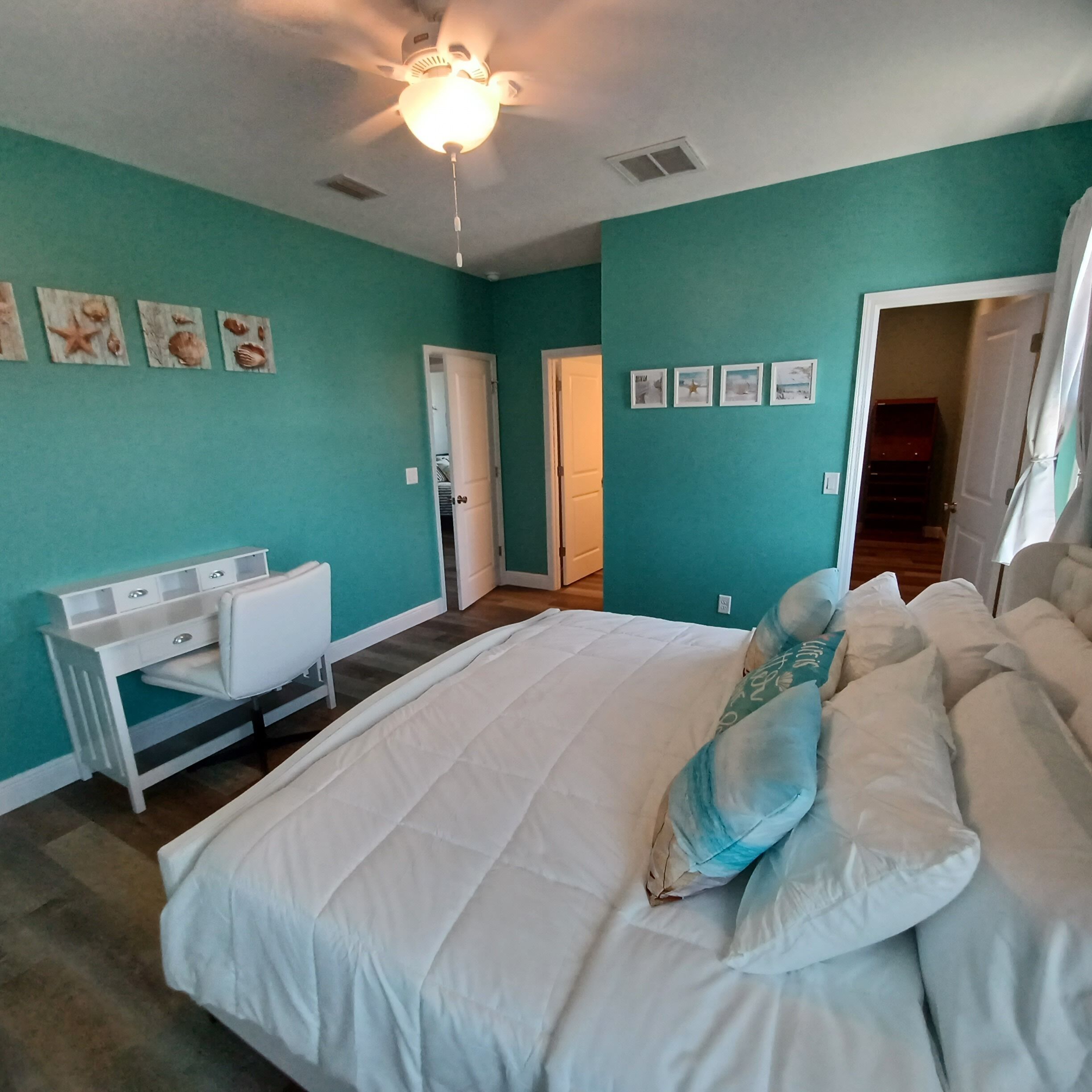 Une chambre avec des murs de couleur turquoise, un lit blanc et un ventilateur de plafond.