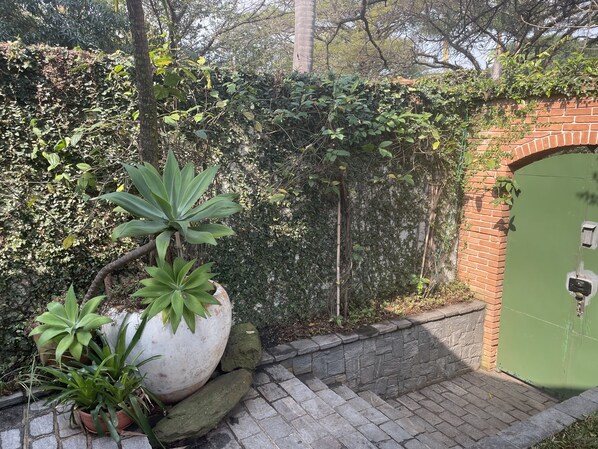 Un muro de ladrillo con una verja verde, plantas en macetas y un camino de piedra.