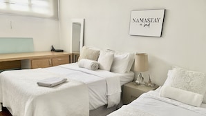 A hotel room with two beds, a bedside table with a lamp, a mirror, and a wall-mounted sign that reads "NAMASTAY in bed".
