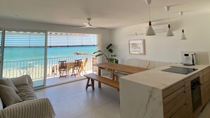 A modern kitchen with a marble countertop, a dining area with a wooden table, and a balcony with a view of the sea. - Appartement Luxe, 1ère Ligne sur la Plage, T3, Climatisé, Terrasse,plancha,wifi (Palavas-les-Flots)