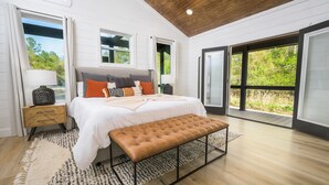Une chambre à coucher avec un lit, un banc, des tables de chevet et de grandes fenêtres.