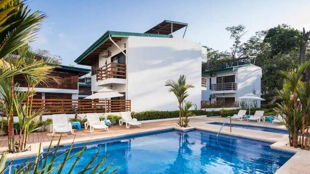 A modern hotel with a swimming pool, multiple balconies, and lounge chairs.