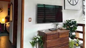 A modern living room with a wooden ceiling, a mounted surfboard, a large flat-screen TV, a peace sign artwork, and a wooden cabinet with potted plants.