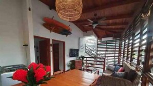 A dining area with a wooden table and chairs, a vase of red flowers, and a wicker ceiling fan.