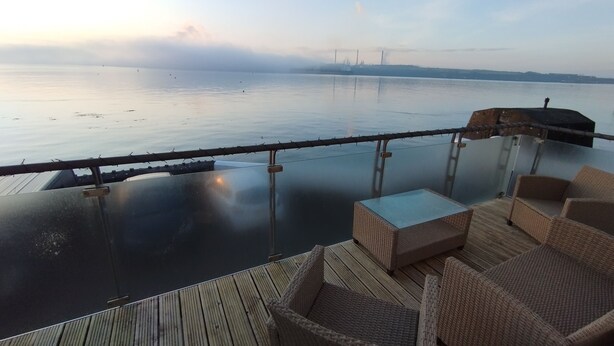 Eine Holzterrasse mit Korbmöbeln mit Blick auf ruhiges Gewässer.