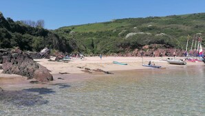 Ein Strand mit klarem, flachen Wasser, felsigen Abschnitten und einer hügeligen Kulisse.