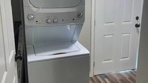 A compact, white laundry room with a front-loading washer and dryer, a door to the right, and a wooden floor.