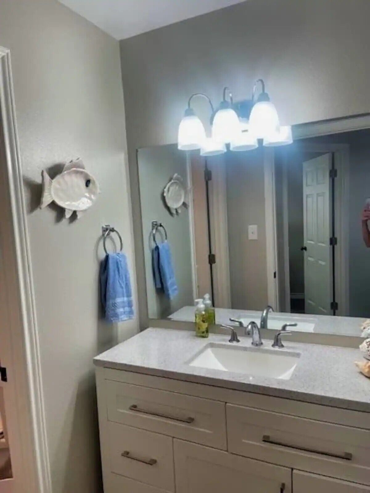 A bathroom with a large mirror, three wall-mounted lights, a sink, and two towels hanging on hooks.