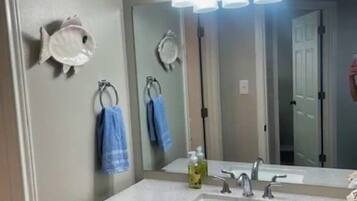 A bathroom with a large mirror, three wall-mounted lights, a sink, and two towels hanging on hooks.