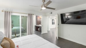 A modern hotel room with a bed, a ceiling fan, a large TV, and a sliding glass door leading to a balcony. - Pool and Beautiful Tempe - Scottsdale Home! (Tempe)