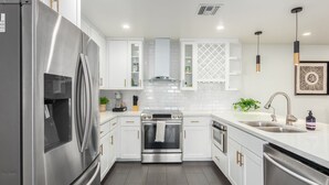 A modern kitchen with stainless steel appliances, white cabinetry, and a central island with a sink and countertop. - Pool and Beautiful Tempe - Scottsdale Home! (Tempe)