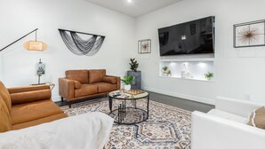 A modern living room with a brown sofa, a white armchair, a patterned rug, and a flat-screen TV mounted on the wall. - Pool and Beautiful Tempe - Scottsdale Home! (Tempe)