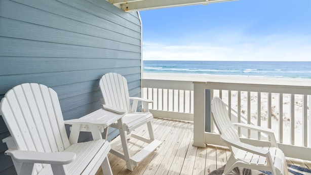 A covered deck with two Adirondack chairs facing a beach.