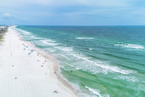 Ein Strand mit weitem Sandstreifen, Wellen und blauem Himmel.