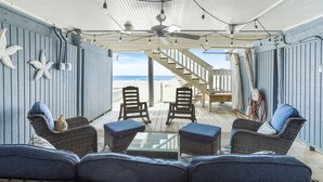 A covered outdoor seating area with wicker furniture and a glass table, overlooking a beach.