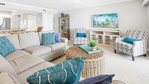 A living room with a beige sofa, patterned armchairs, a wicker coffee table, and a painting on the wall.